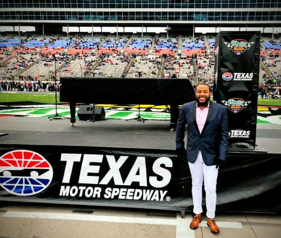 Lewis Warren Jr. poses with piano in front of a banner that reads "Texas Motor Speedway."