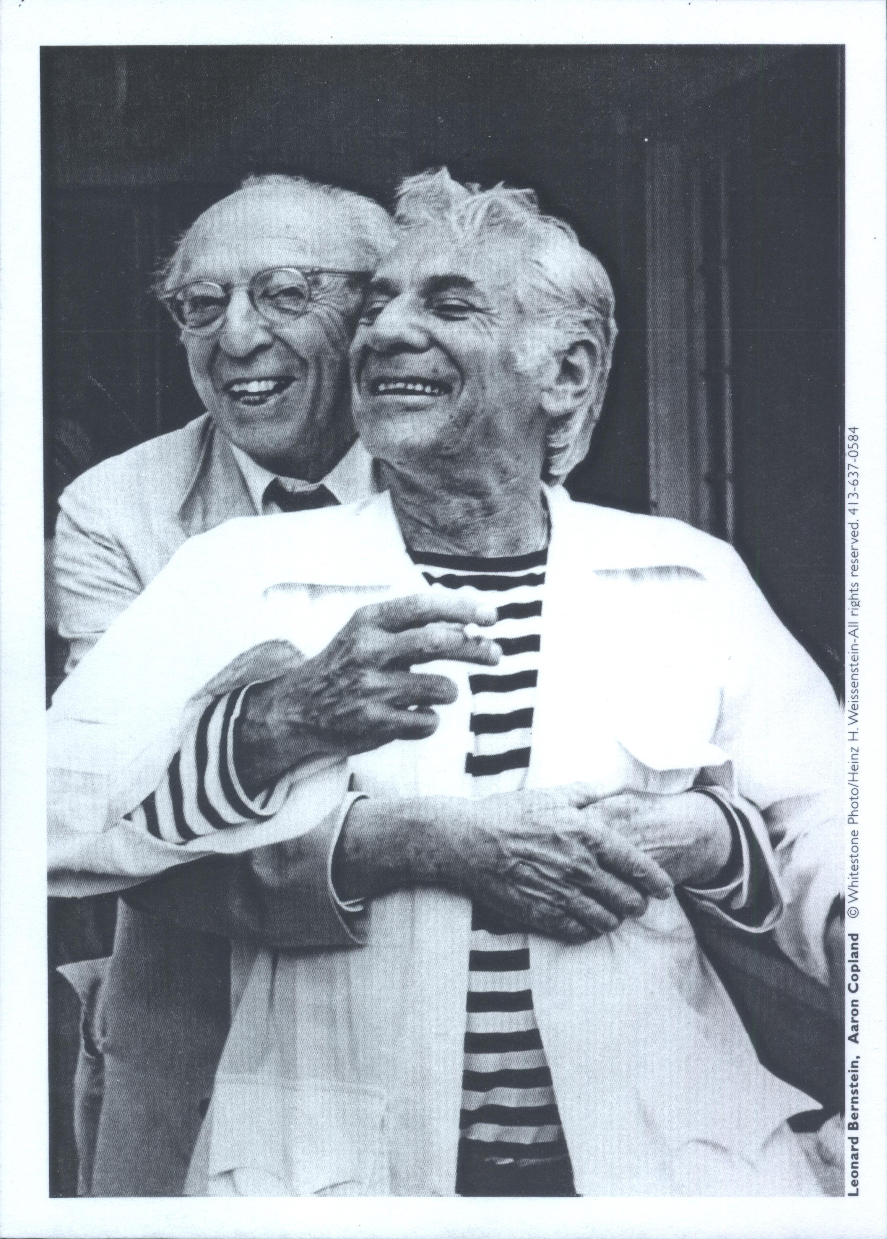 Aaron Copland hugs Leonard Bernstein. Both men are smiling.