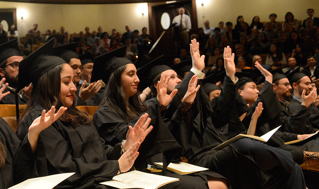 Graduates raise their hands in Jordan Hall