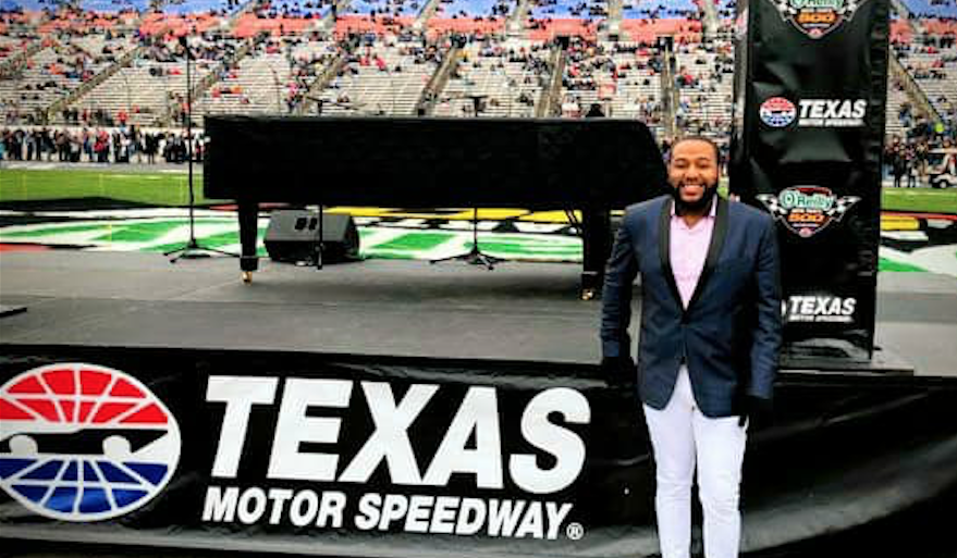 Lewis Warren Jr. poses with piano in front of a banner that reads "Texas Motor Speedway."