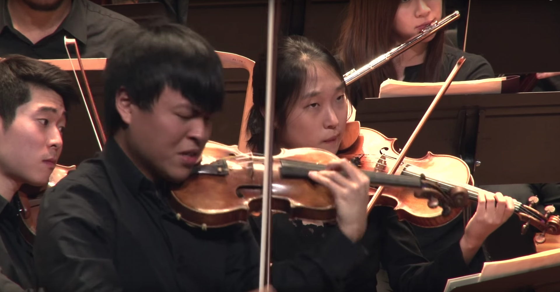 Luke Hsu plays the violin as a soloist with NEC Philharmonia behind him.