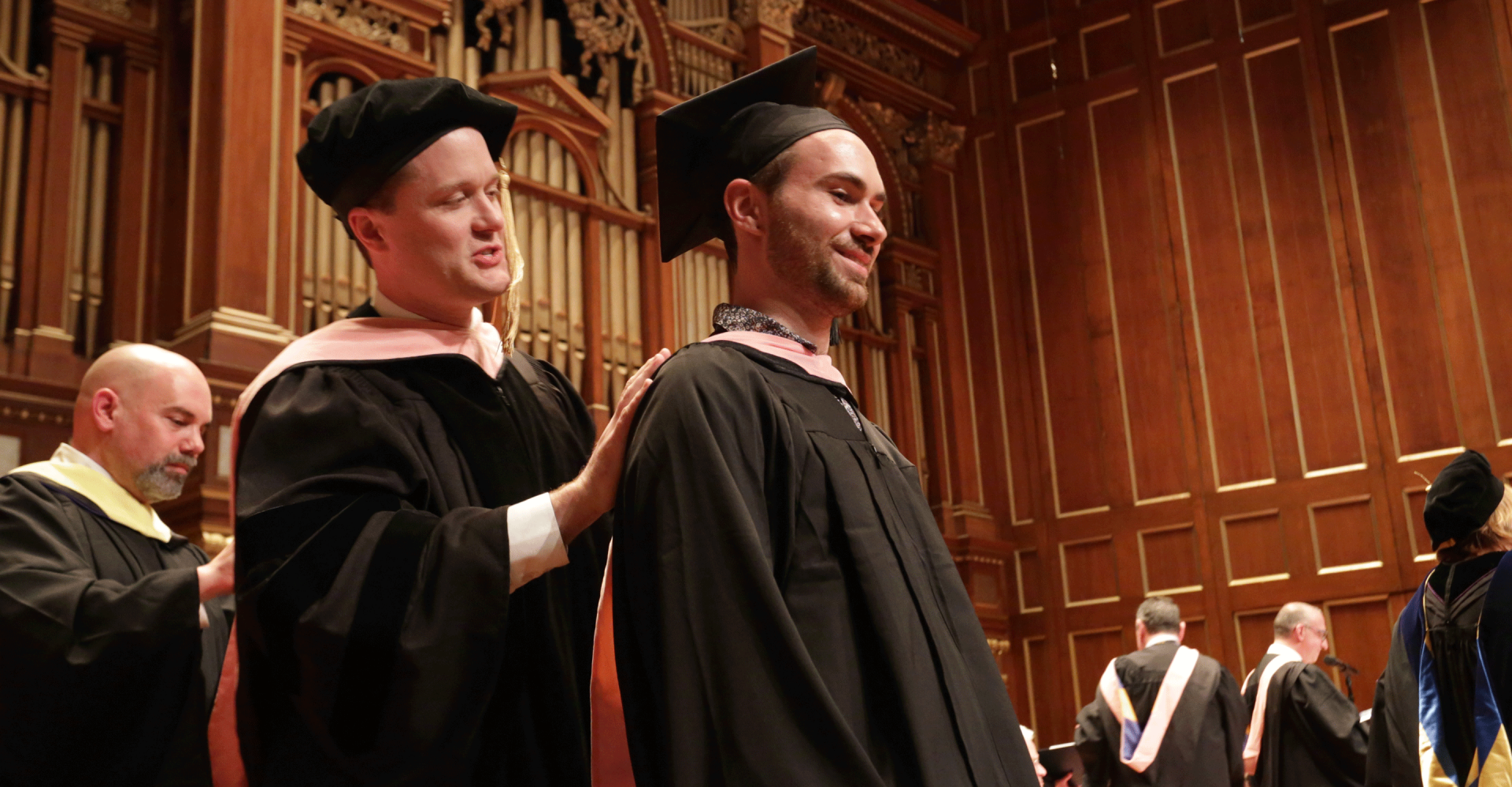 Alex Powell awards a master's hood to a graduate on the Jordan Hall stage