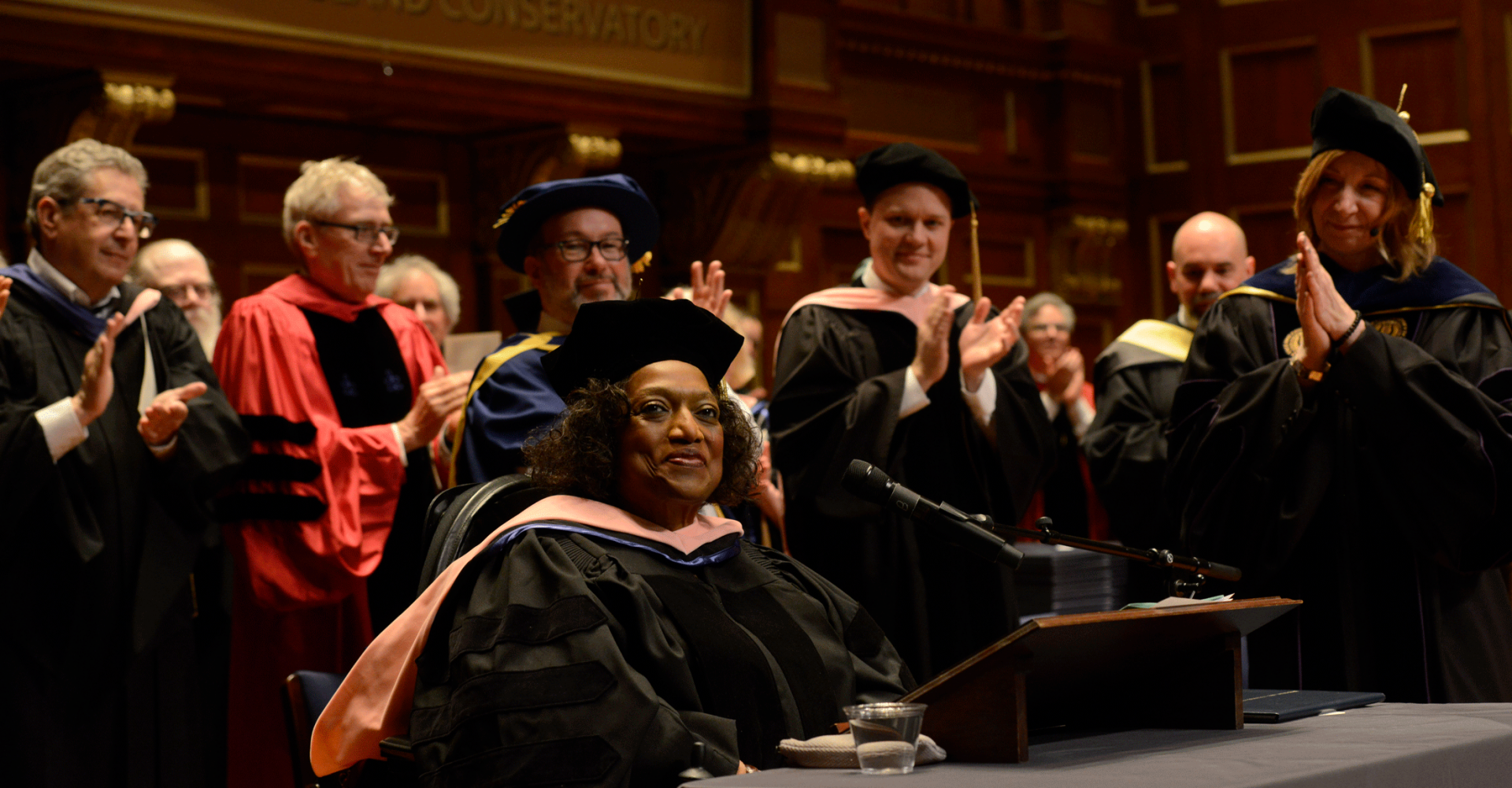 Jessye Norman smiles on the Jordan Hall stage while faculty applaud after she gave a keynote address