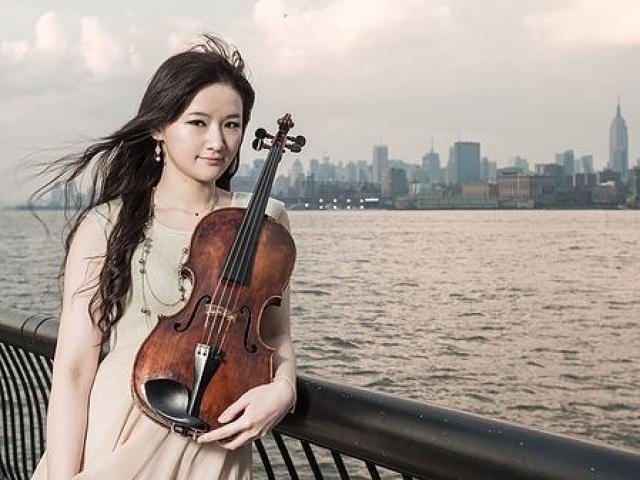 Ting-Ru Lai with her viola in front of a city landscape and a body of water