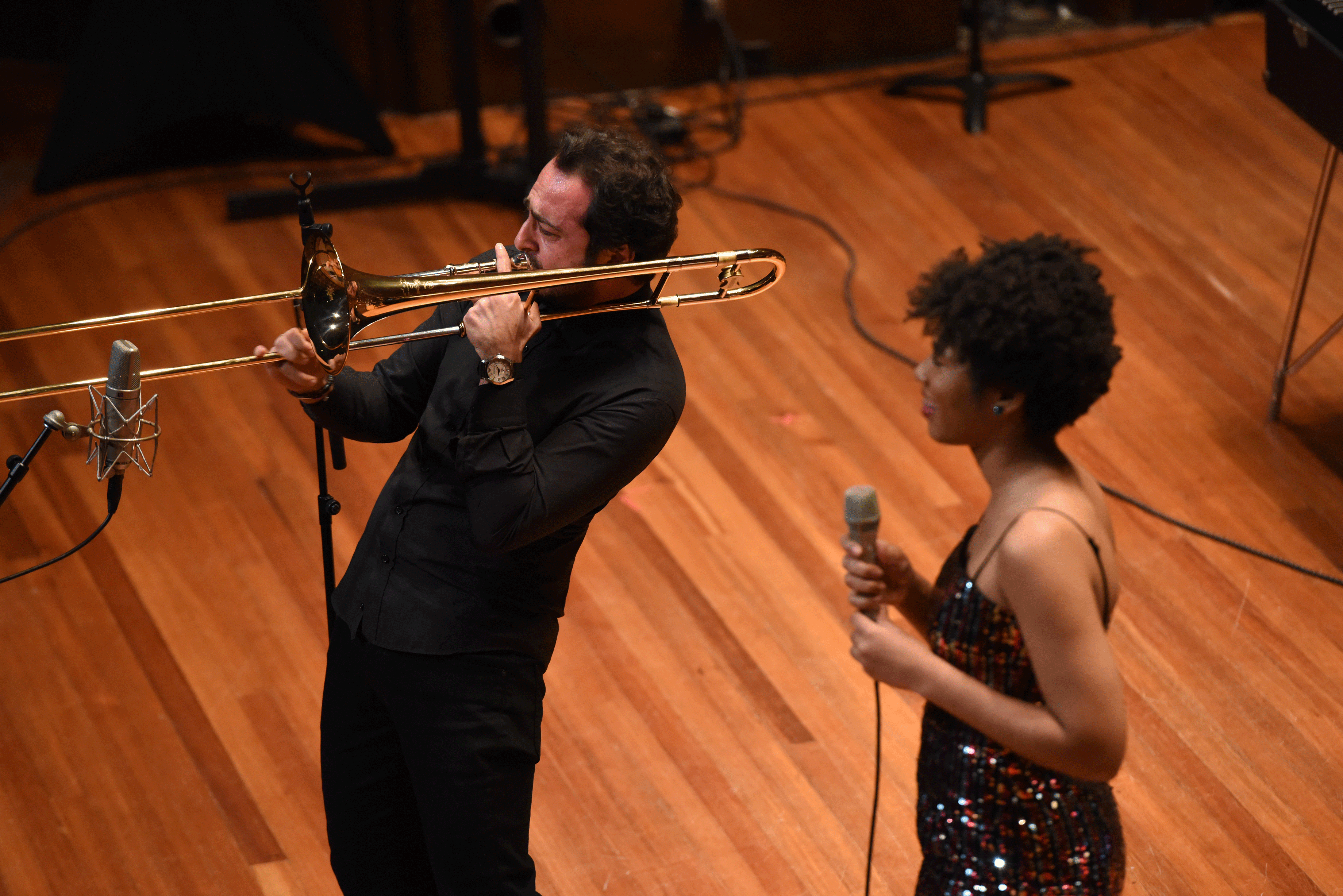 Bulut Gulen plays trombone while Darynn Dean holds a microphone