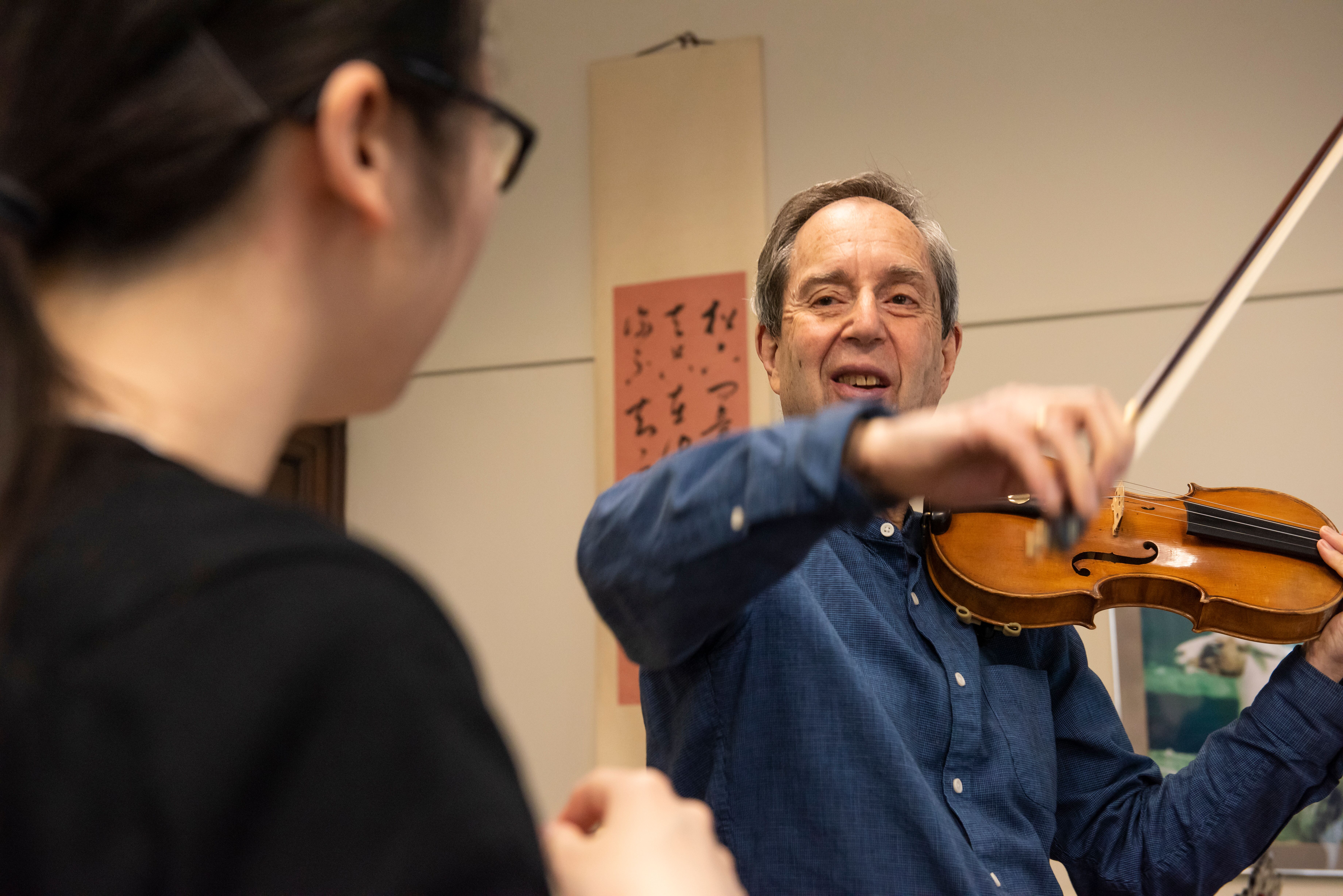 Donald Weilerstein holds his bow over his violin and smiles while teaching a student