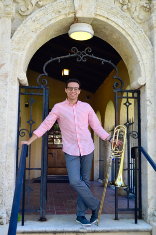 Felix Padilla with bass trombone, standing in an ornate archway