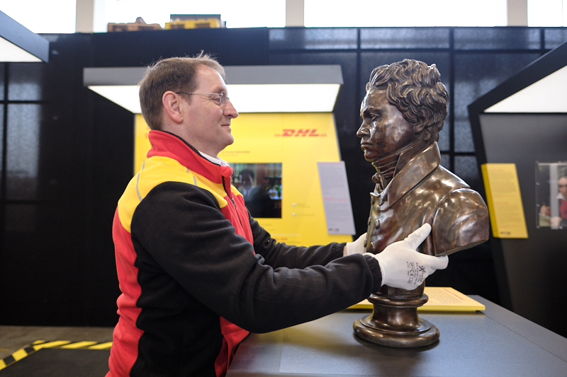 DHL employee smiles and looks a bust of Beethoven in the eye.