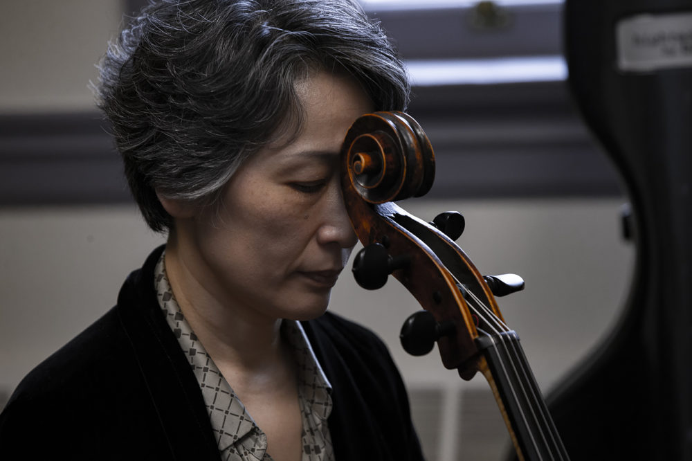 Yeesun Kim closes her eyes and meditates, resting her cello scroll against her forehead.