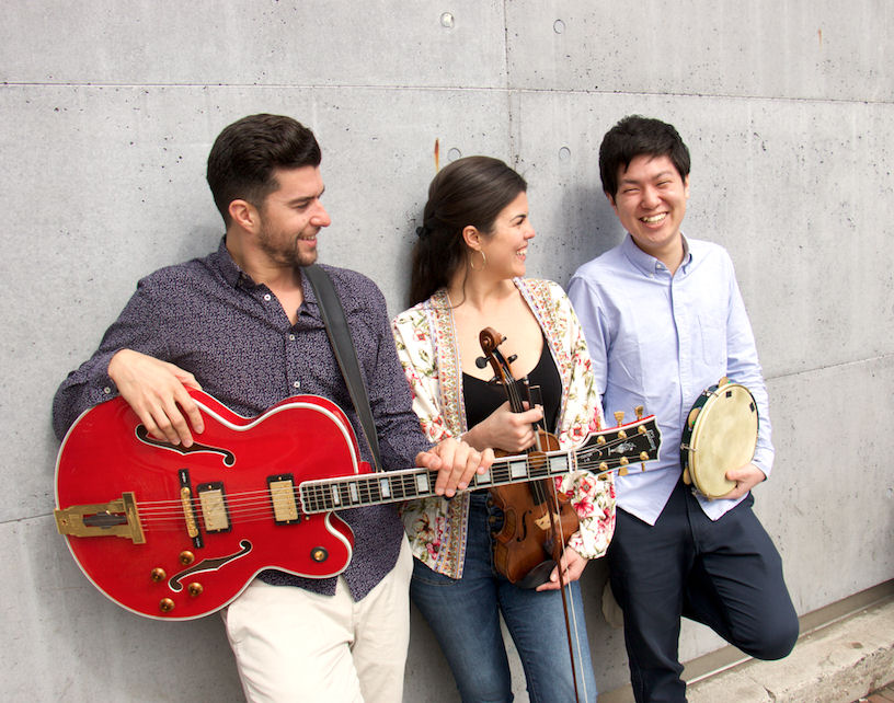 Julia Bomfim trio smile and lean against a wall with their instruments