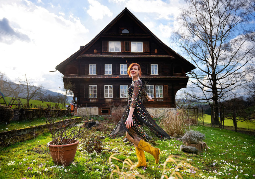 Gabriela Martina twirls in a black dress, smiling in front of a farm house, blue sky, and green fields.