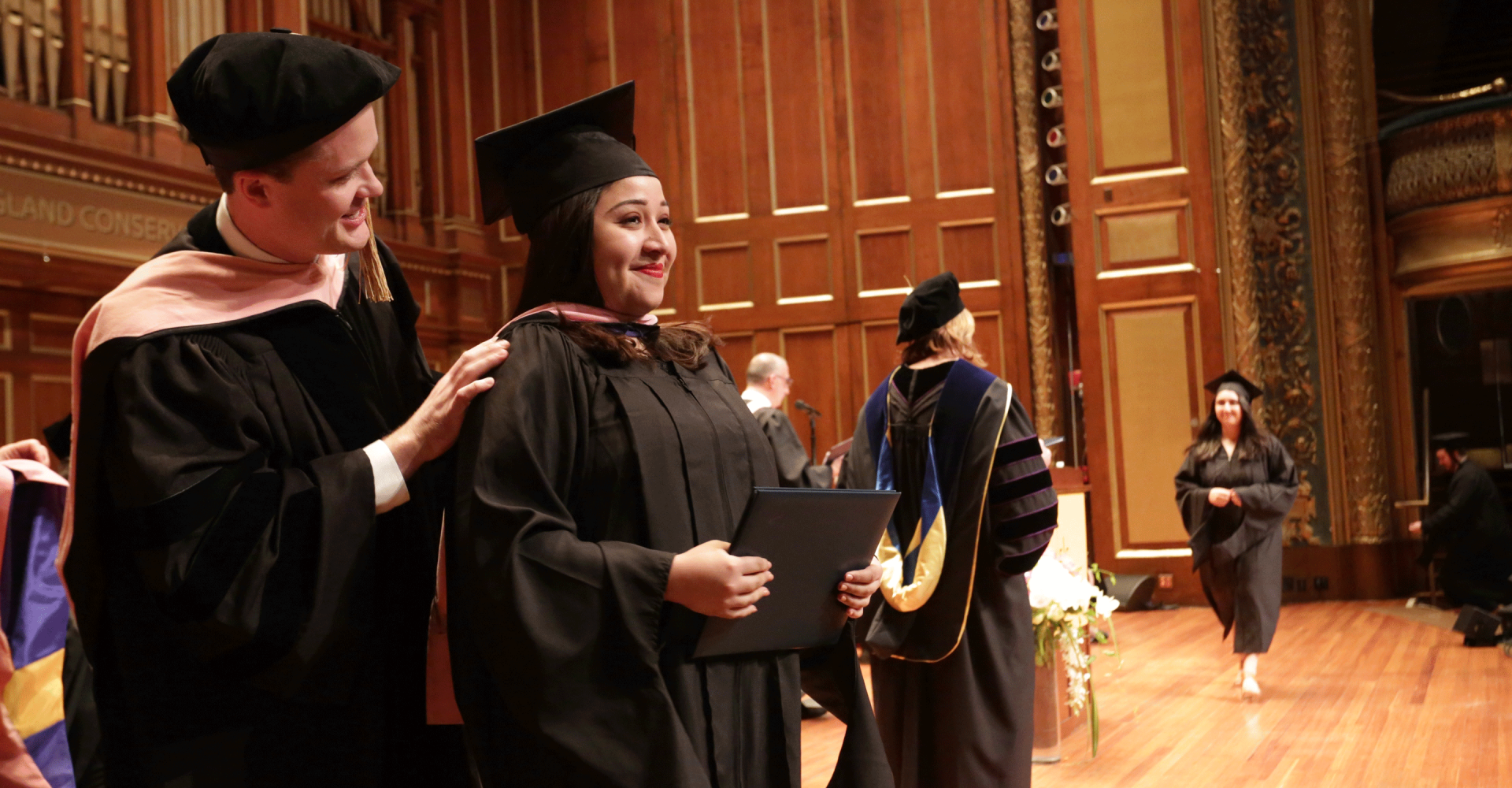 Julimar Alarcon smiles on the Jordan Hall stage as she receives her master's hood at commencement