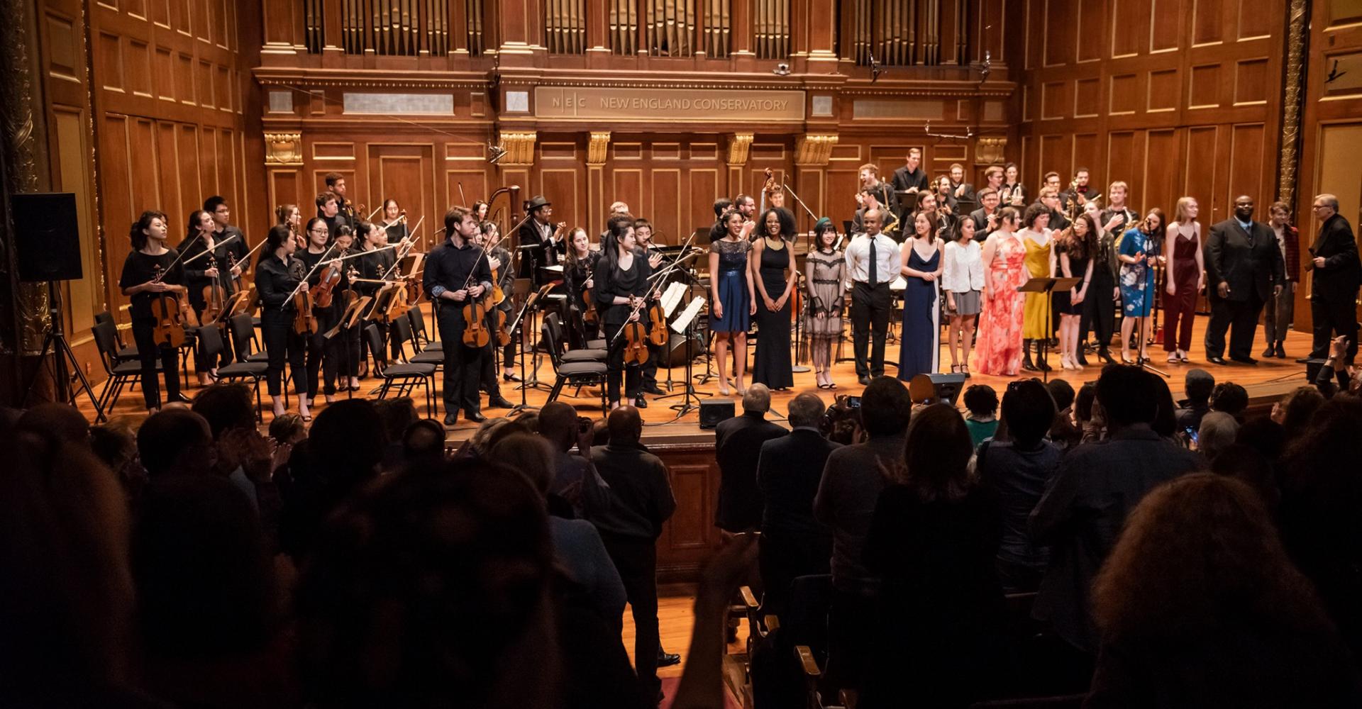 Performers take a bow in Jordan Hall while the audience stands and applauds