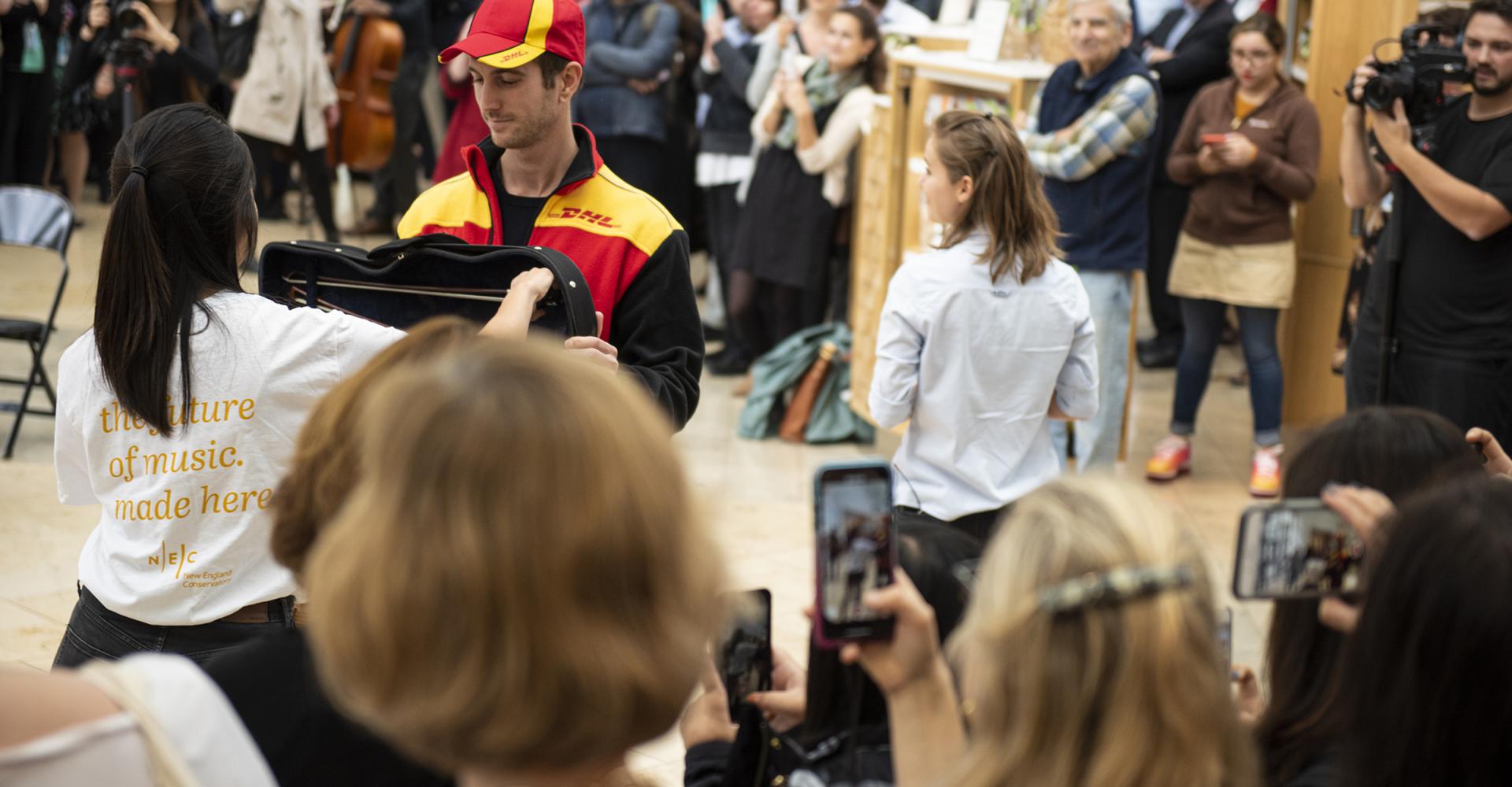 A DHL driver delivers a violin to a waiting musician.