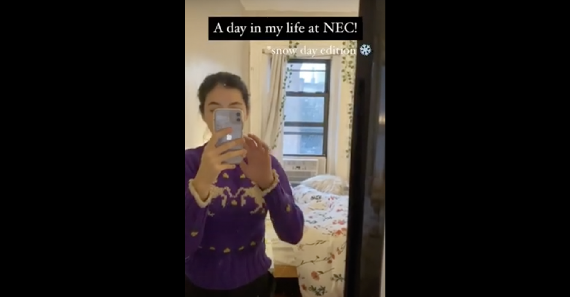 Yi Mei videos herself in the mirror of her room, with snow falling through the window behind her. The text on the screen says "A day in my life at NEC: Snow Day Edition"