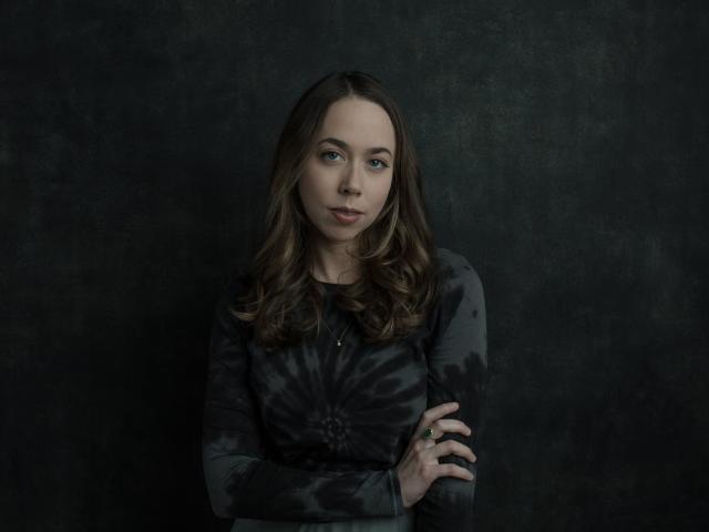 Sarah Jarosz is pictured against a dark background. She is wearing black and looking to the side.