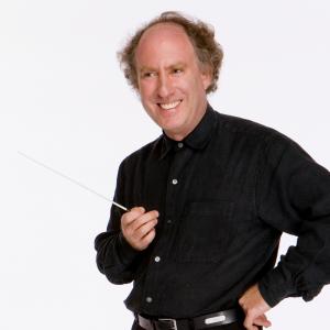 Jeffrey Kahane smiles and looks to the side while holding his conductor baton, with one hand on hip.