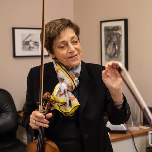 Miriam Fried smiles and holds her violin bow while teaching a lesson with a student.