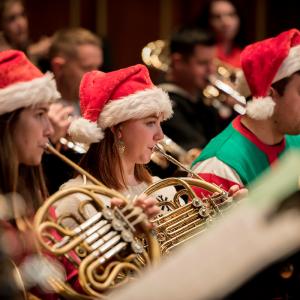 Brass players wear Santa hats and play French horn.