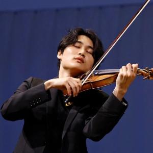 Inmo Yang stand before a blue background, eyes closed, playing violin.