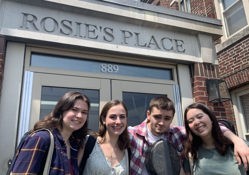 Four students smiling in front of the Rosie's Place building.