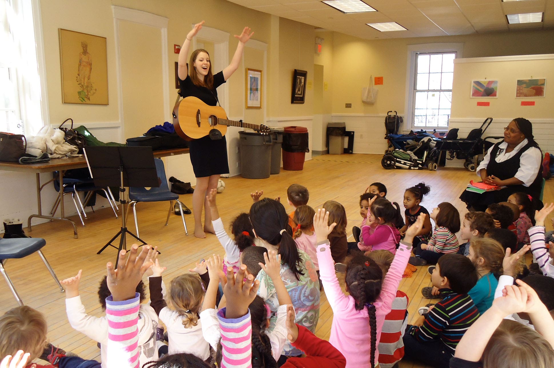 An NEC student holding a guitar and singing for a classroom full of toddlers.