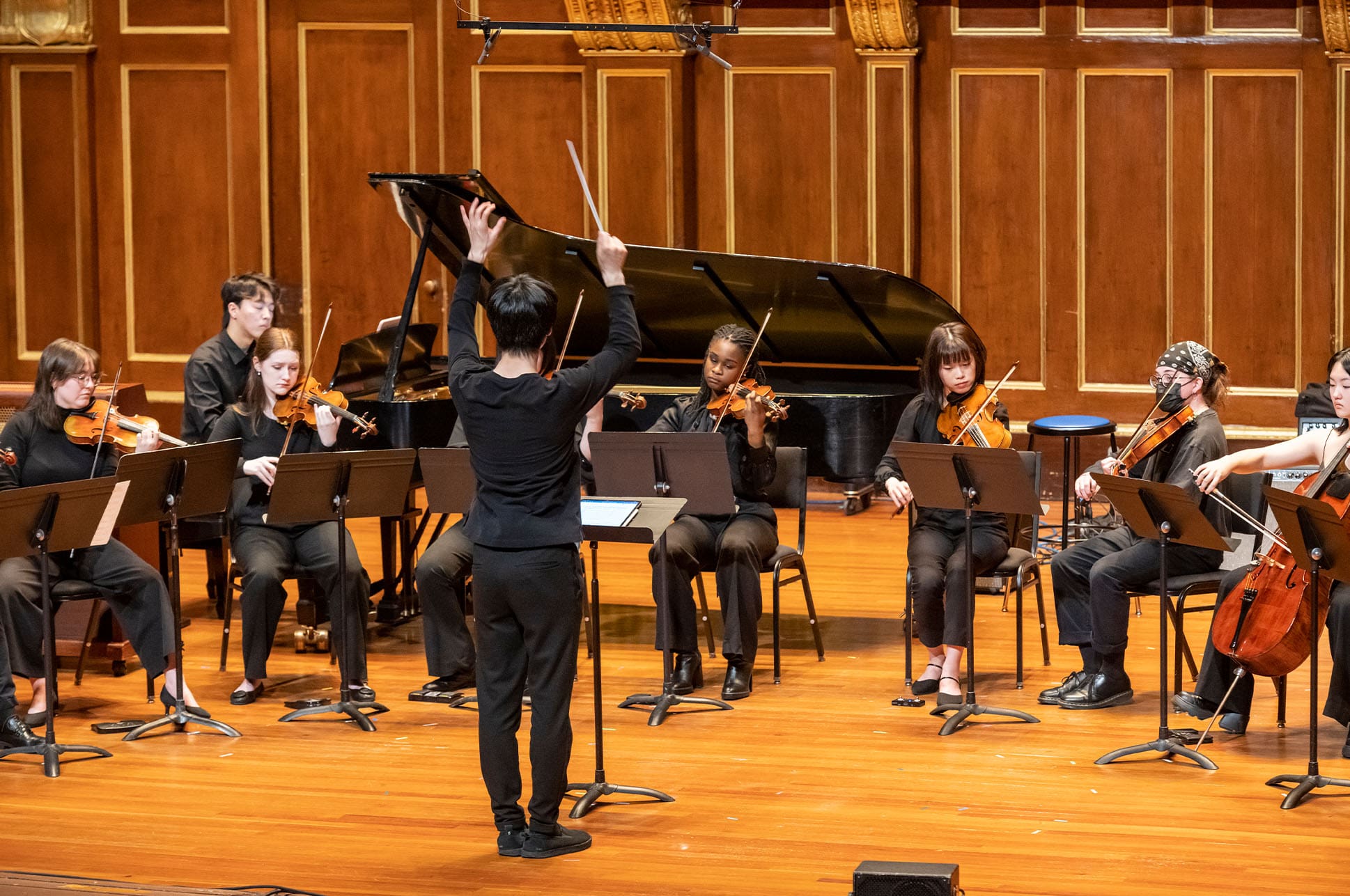 Conductor facing a group of musicians on Jordan Hall stage.