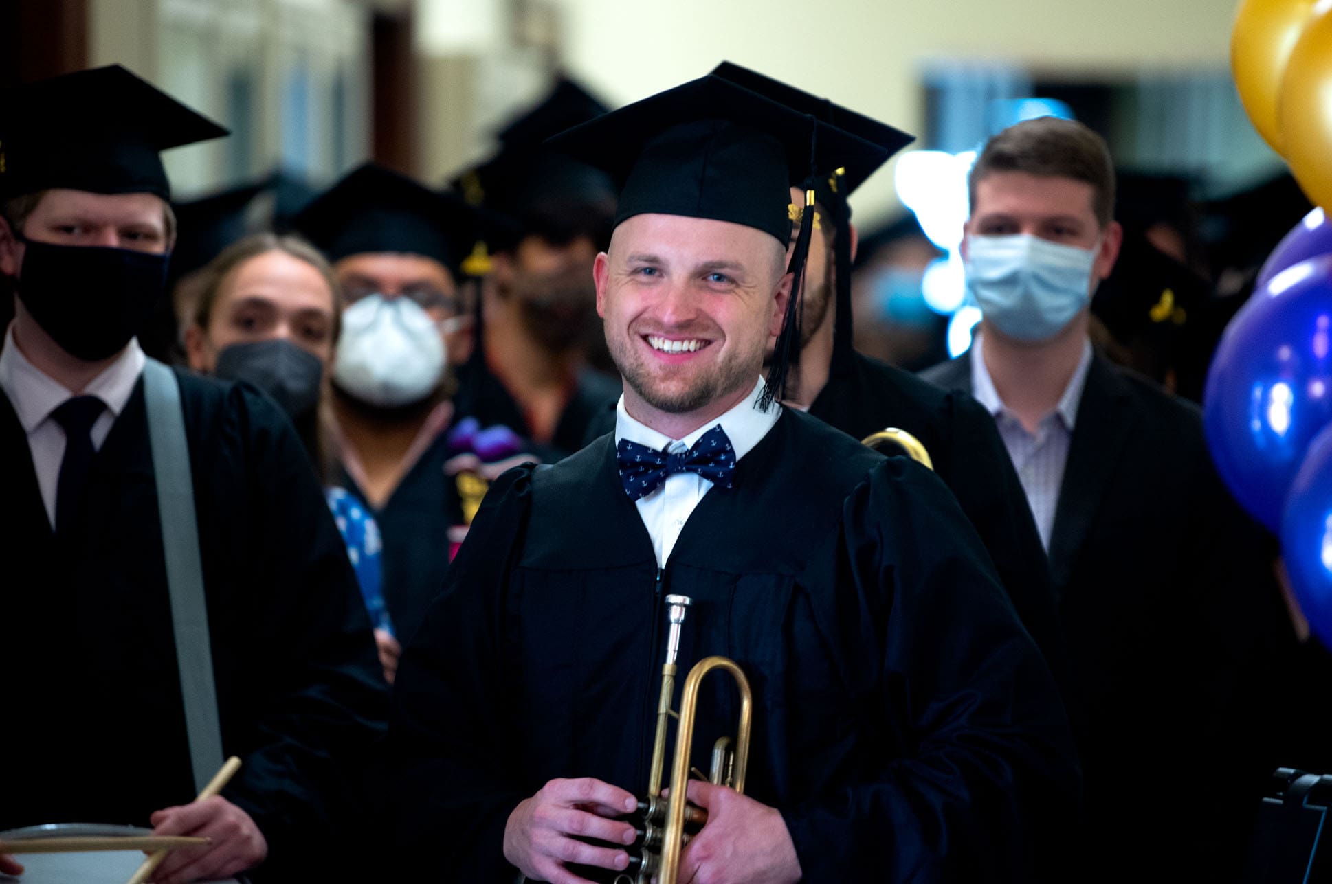 Student in a cap and gown holding a trumpet.