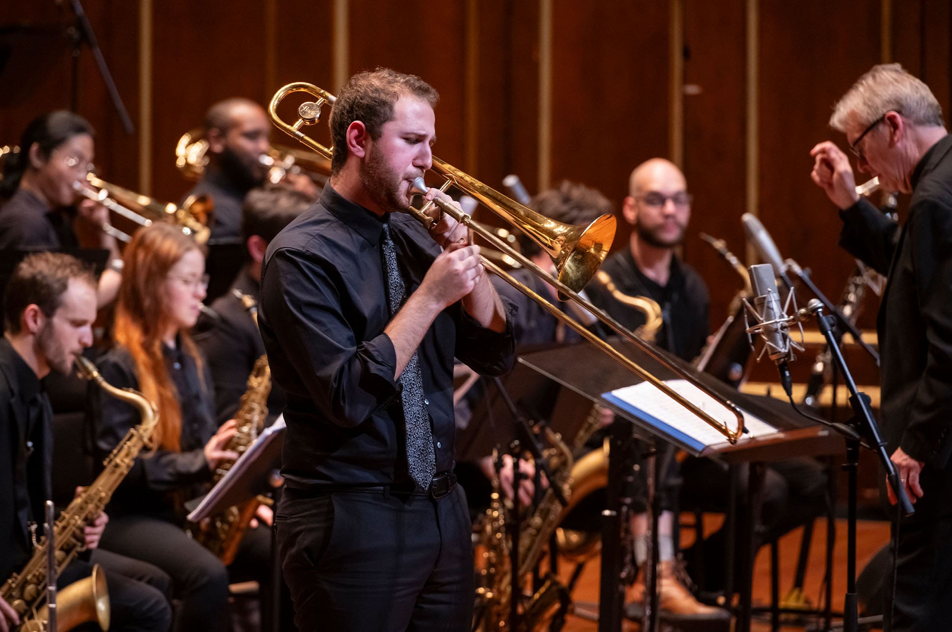 A student playing a trombone in an orchestra on Jordan Hall stage.