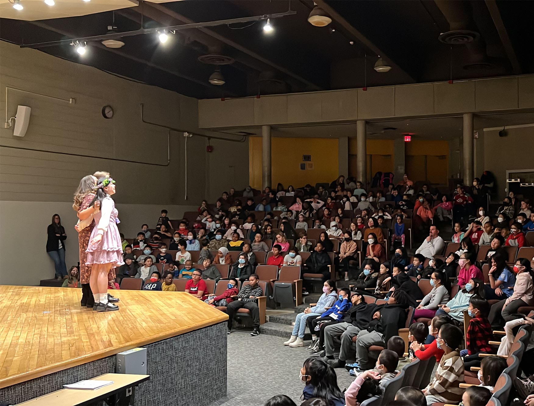 Two children singing on stage to a room full of people.