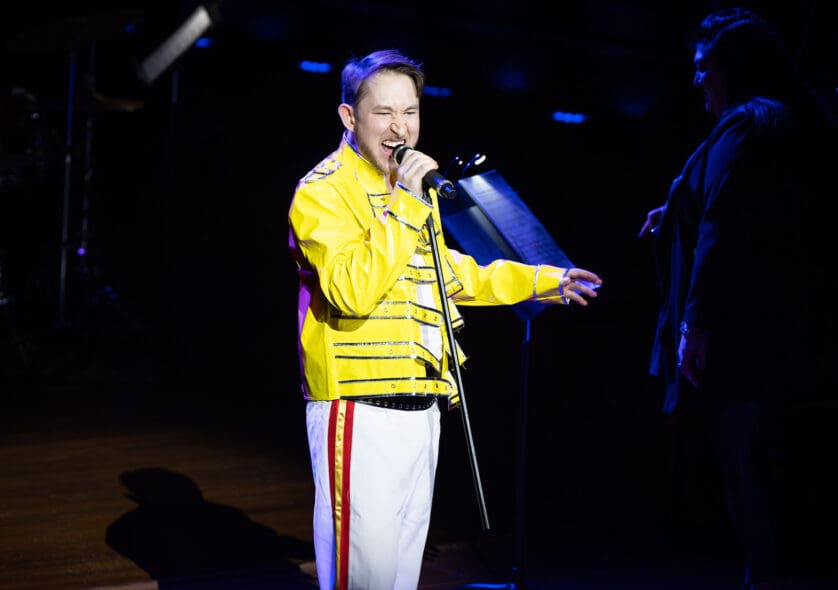 Colin Miller singing on the Jordan Hall stage in a yellow jacket.