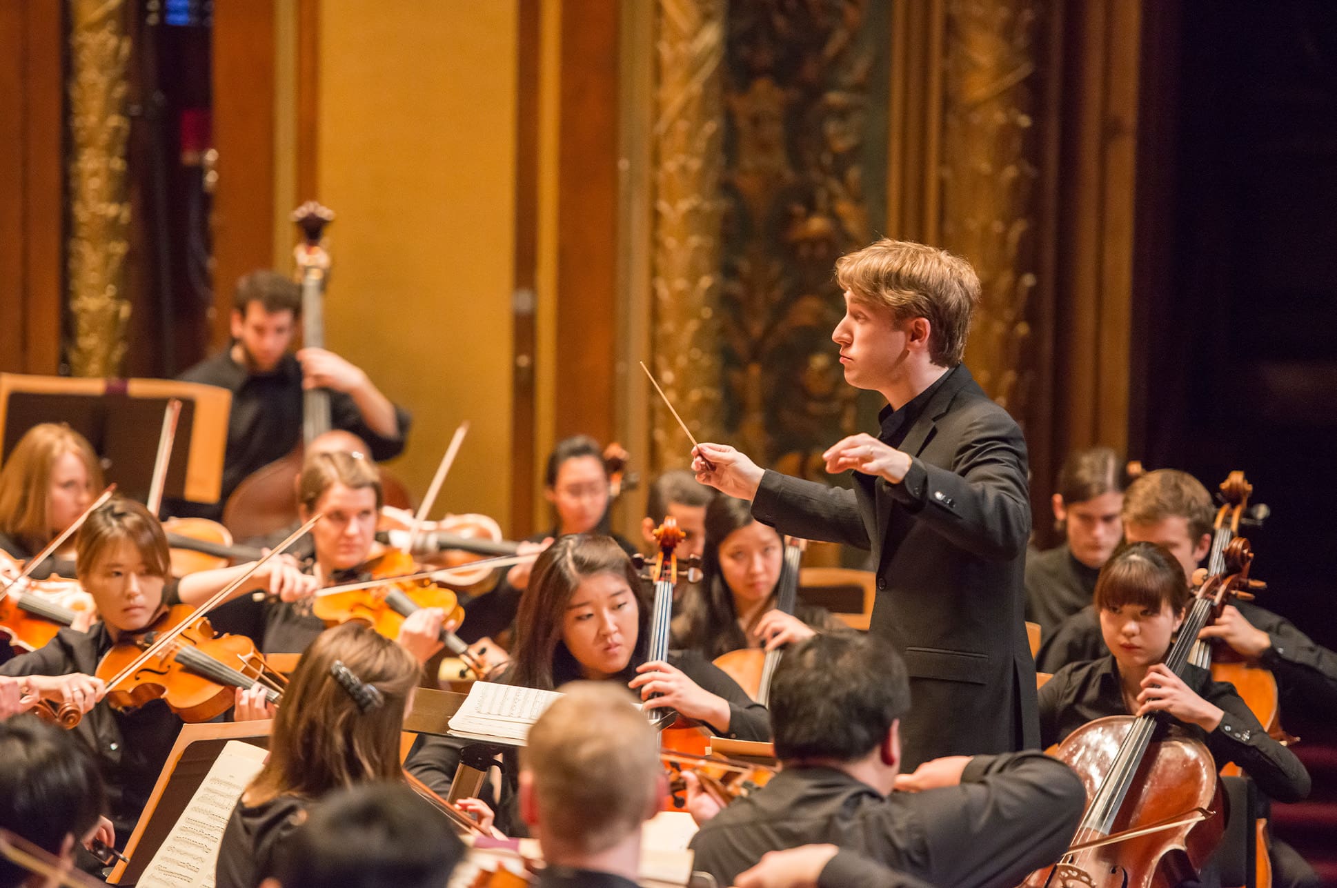 A student conductor leads an orchestra on the Jordan Hall stage
