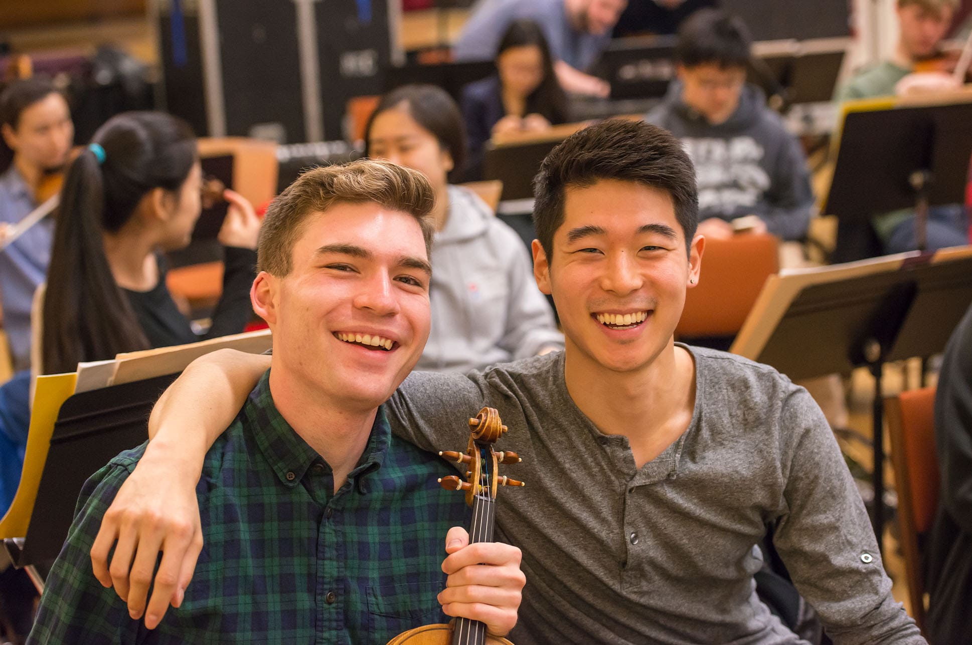 Two students smiling, with one holding a violin.