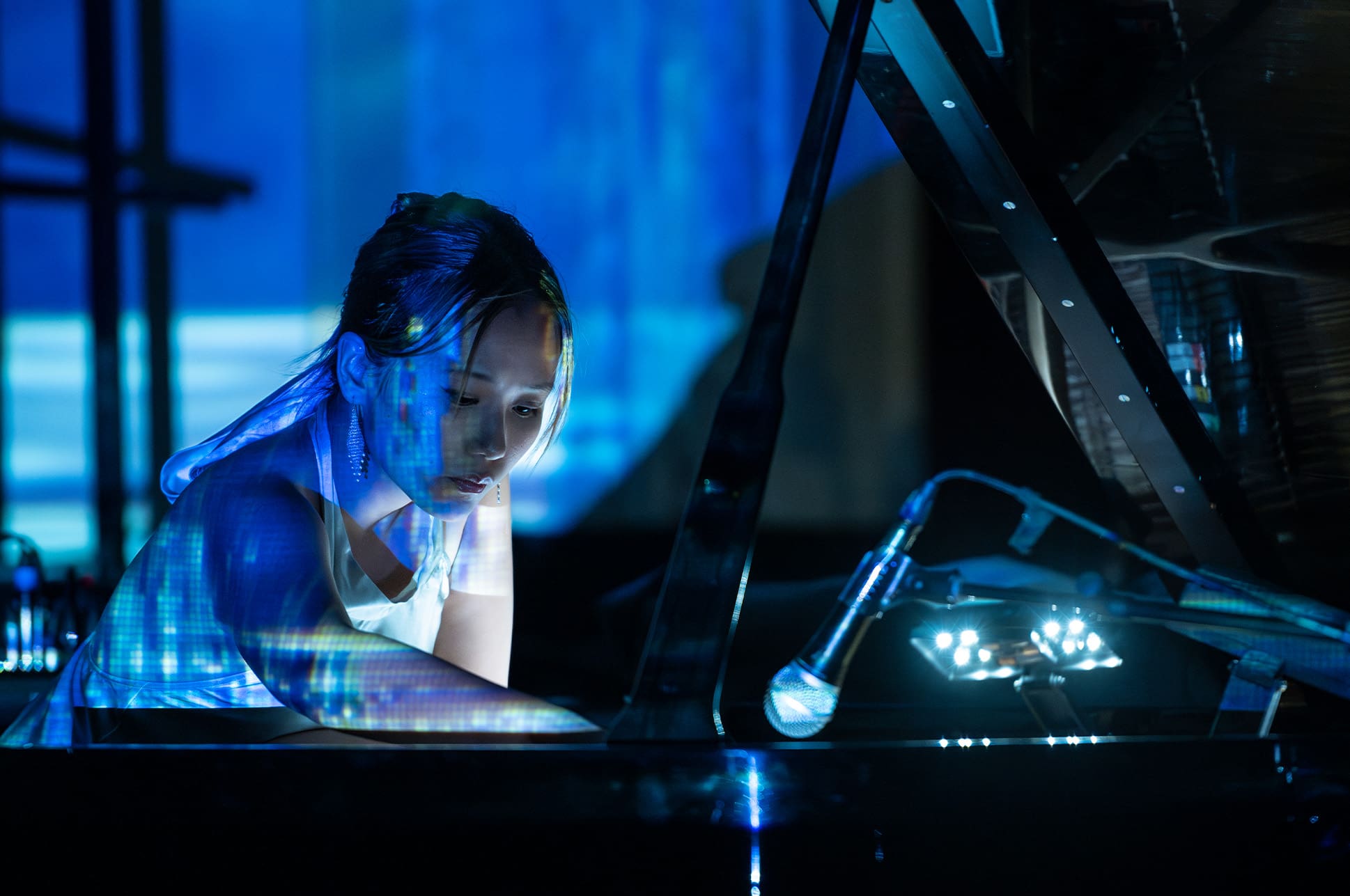 A student performing on piano with colorful projections around her.