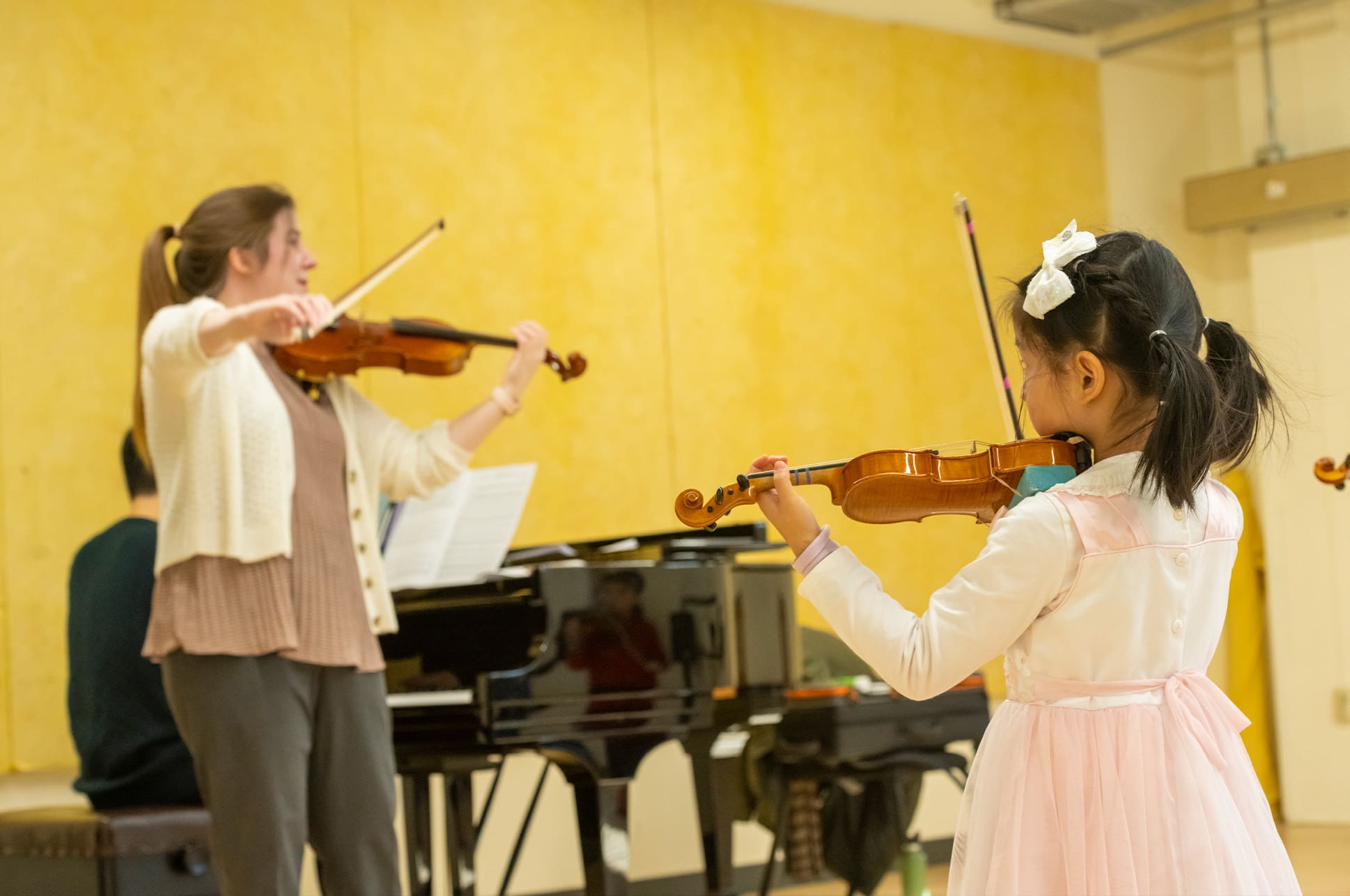 An adult teaching a young child to play violin.