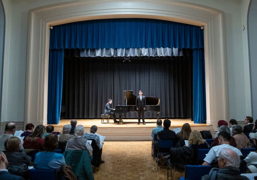 Two students playing piano and singing on Williams Hall stage.
