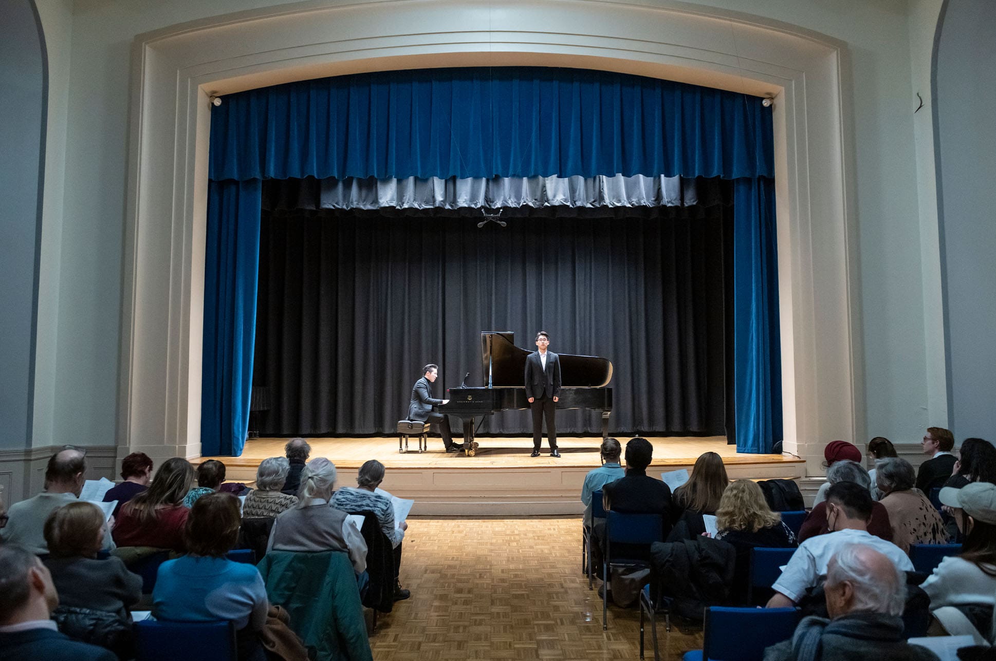 Two students playing piano and singing on Williams Hall stage.