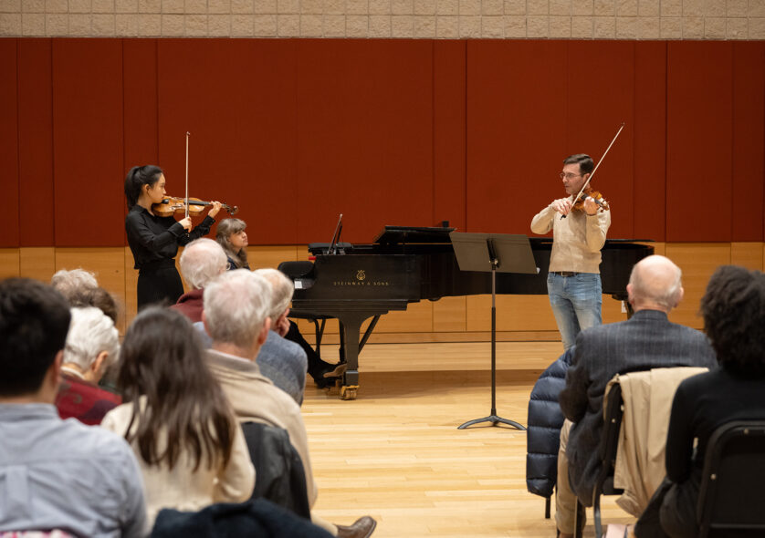 A student and a teacher playing violin while another person plays piano.