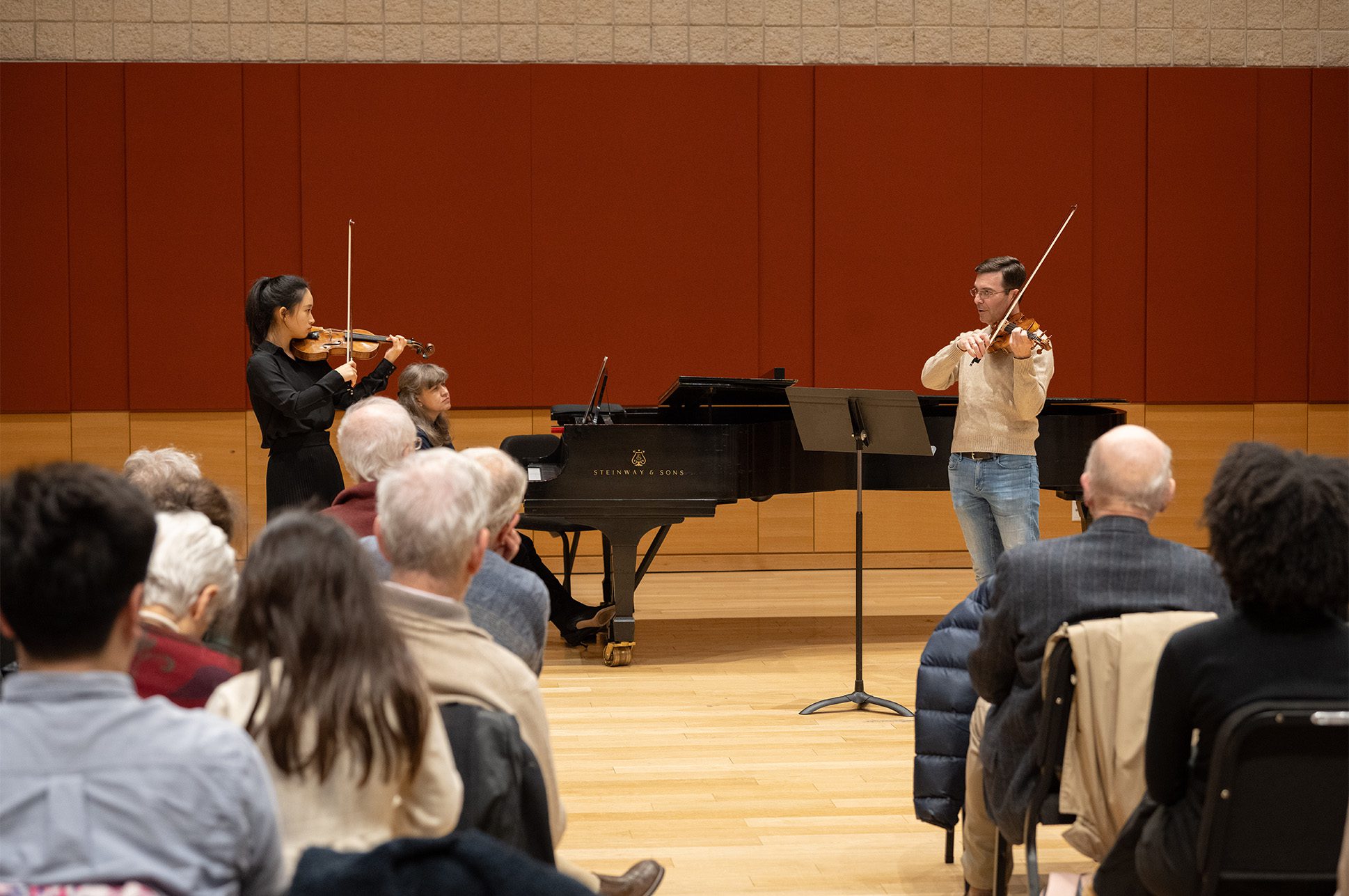 A student and a teacher playing violin while another person plays piano.