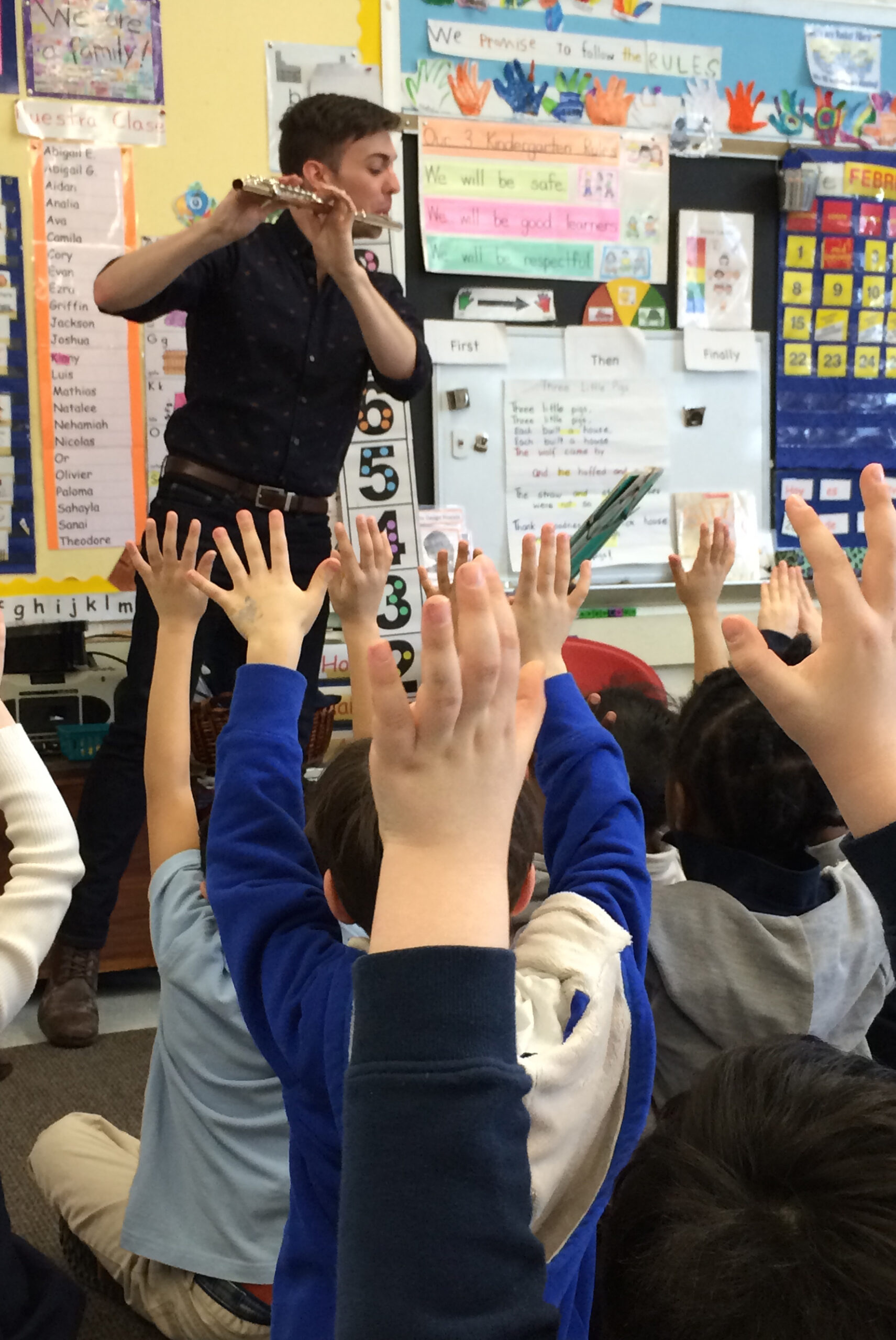 Person playing the flute for a classroom full of children.