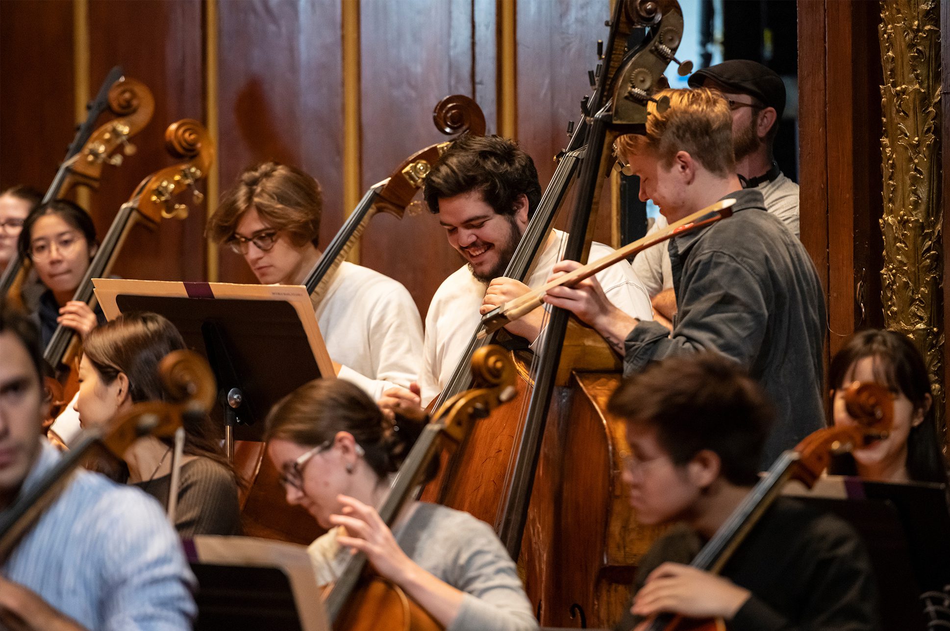 Admitted-Students_Phil+GenevaLewisJHR-NZ7_1873 Students laughing together holding instruments on Jordan Hall stage.