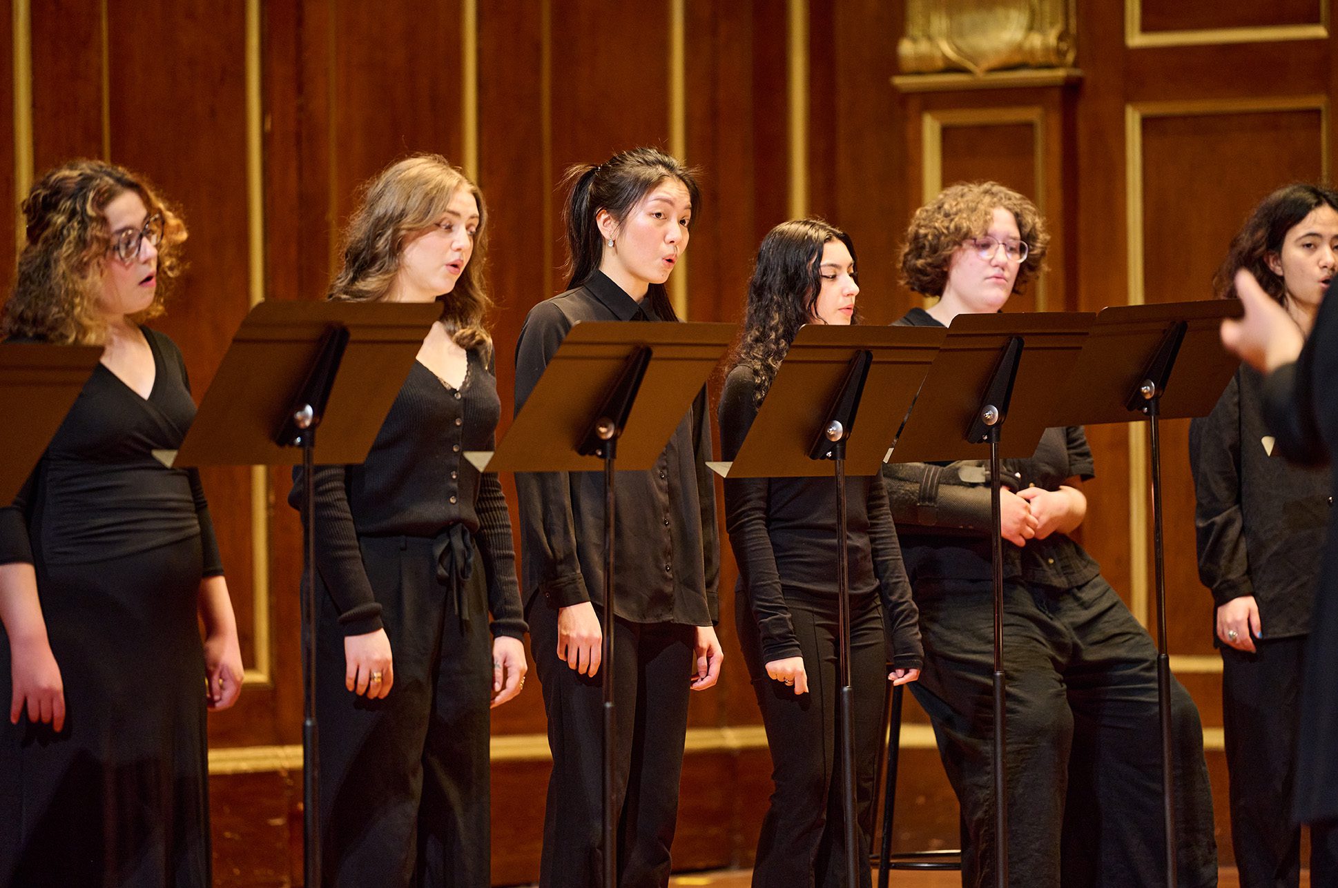 A group of students singing in a choir on the Jordan Hall stage.
