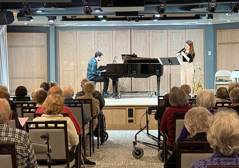 A piano player and wind instrument player on a small stage.