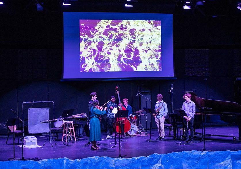 An ensemble of musicians on stage accompanied by a video projection.