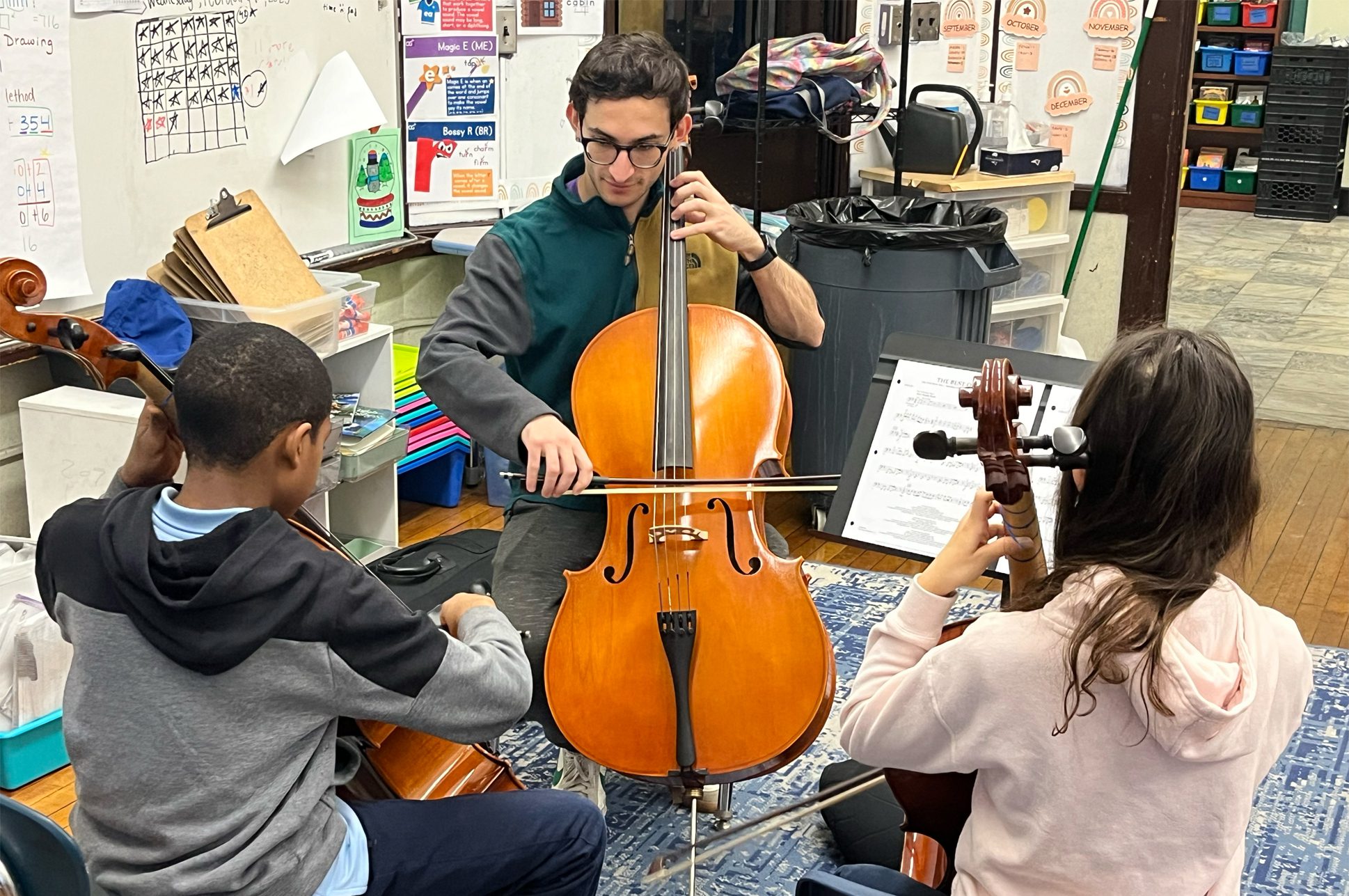 An adult teaching two children how to play the cello.