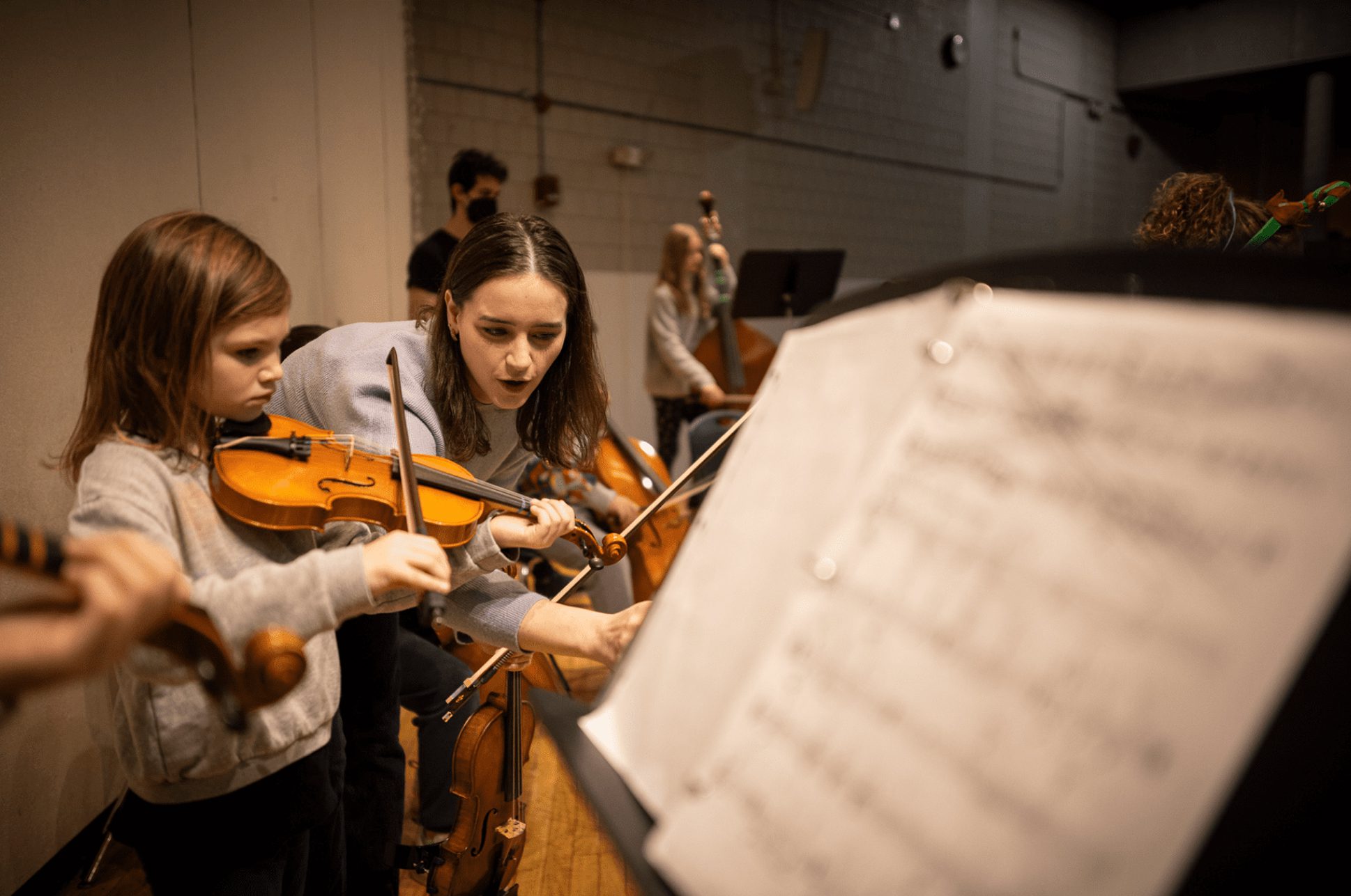 An adult teaching a young child how to play violin.