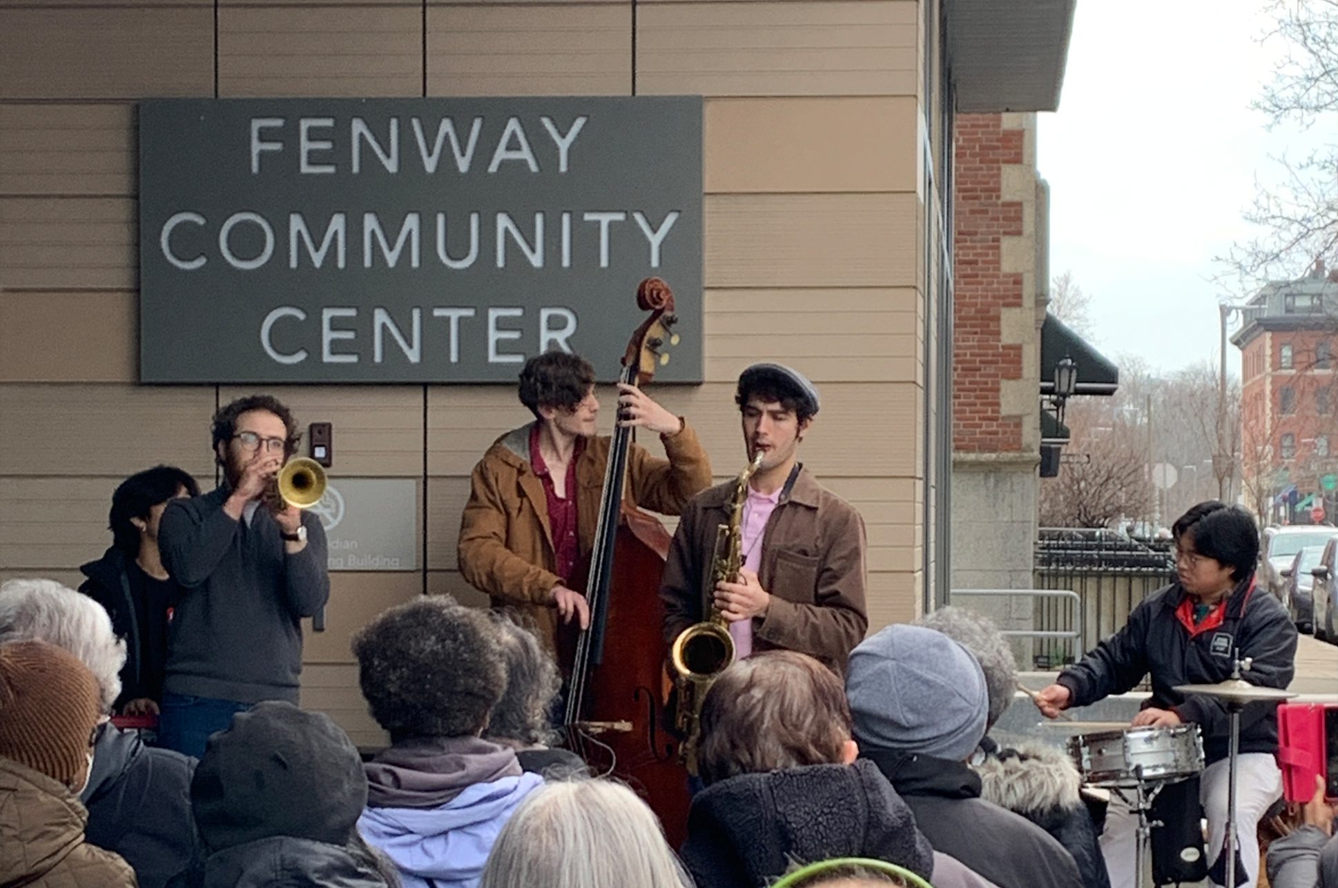 A jazz quartet performing in front of a community center for a crowd of people.