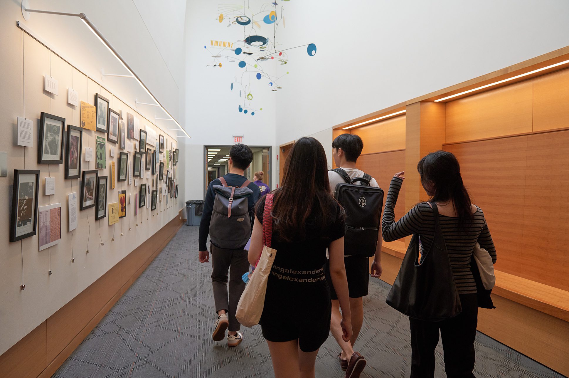 A group of students walking down a hallway with an art exhibit on the wall.