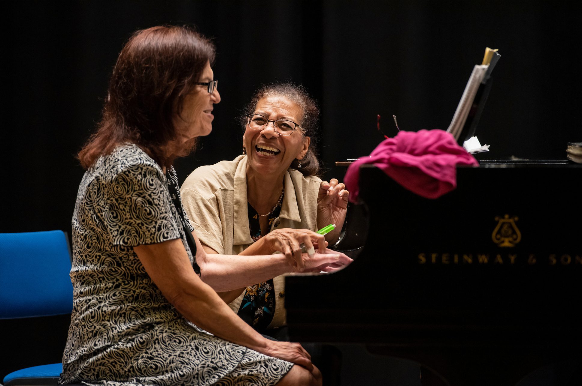 A teacher and a student laughing together at a piano.
