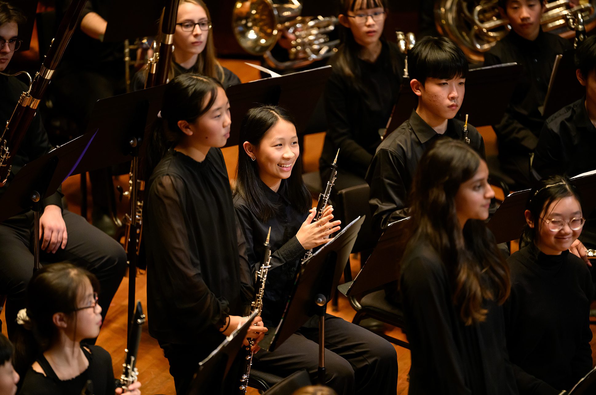 Young woodwind musicians in an orchestra on stage.